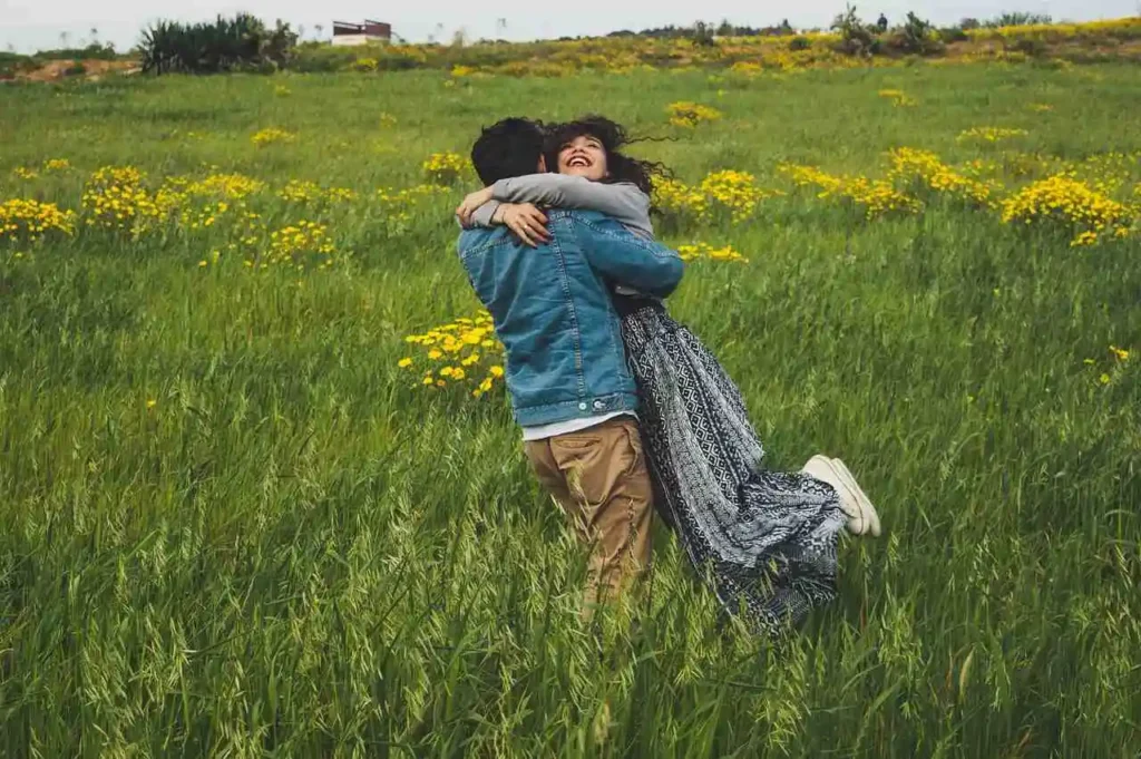 Un garçon tenant joyeusement une fille dans un champ verdoyant avec des fleurs jaunes.