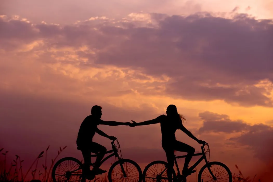 Jeune couple amoureux à vélo, se tenant la main lors d'une belle soirée romantique.