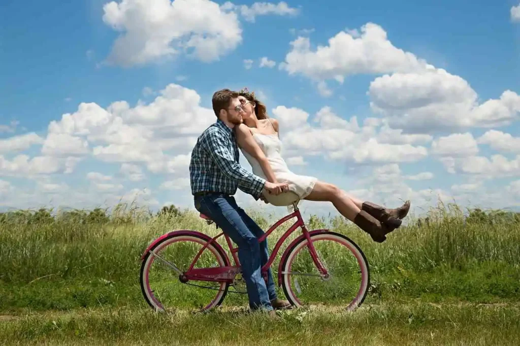 Un petit ami souriant fait du vélo tandis que sa petite amie l'embrasse affectueusement sur le guidon.